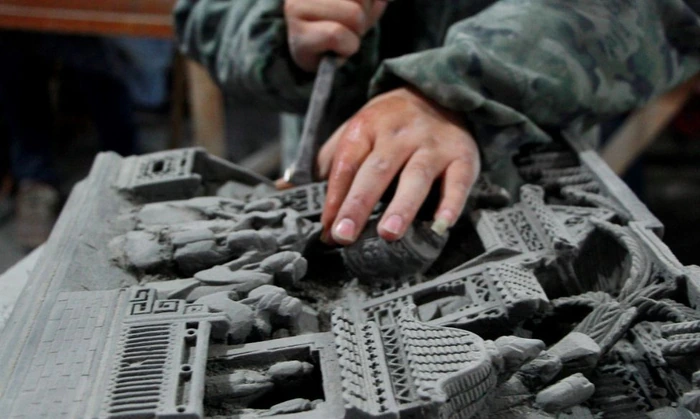 An artisan carving architectural details into grey brick with a hand tool