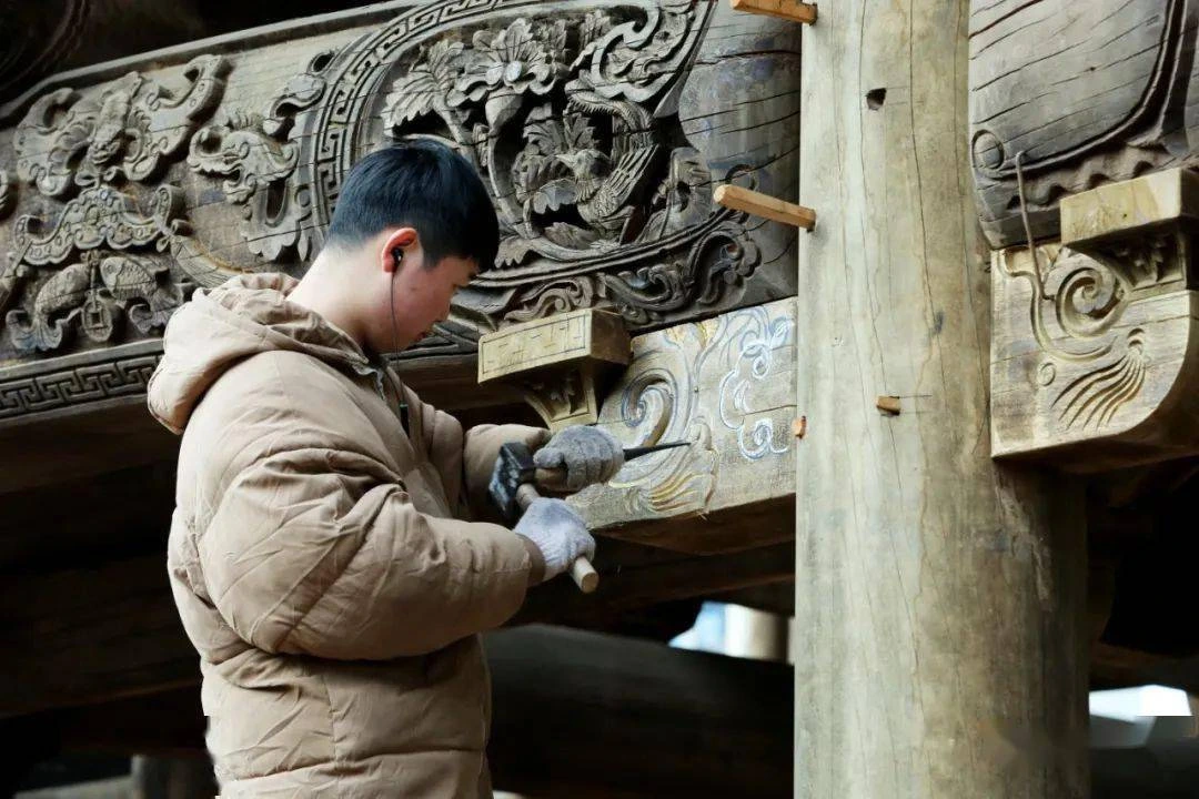 An artisan using a mallet and chisel on an ornate wooden architectural panel