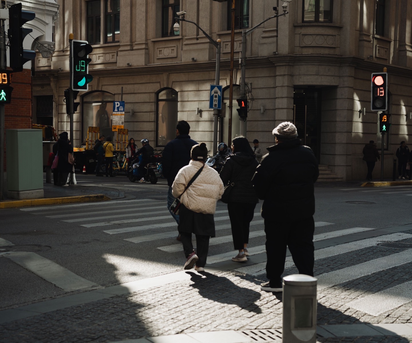 Personas cruzando una calle soleada junto a edificios históricos de Shanghái